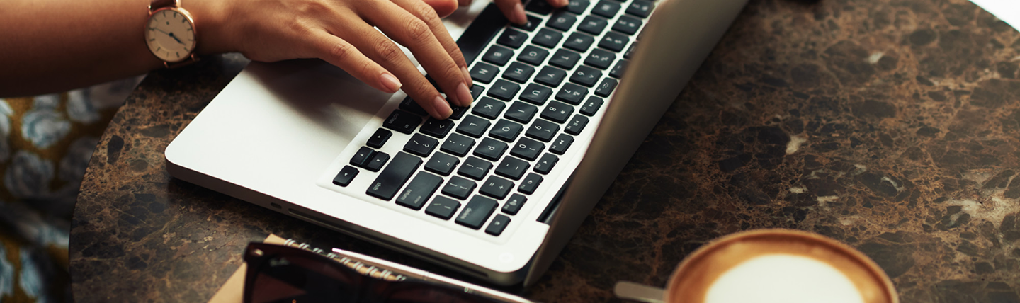 Hands typing on a laptop beside a coffee cup